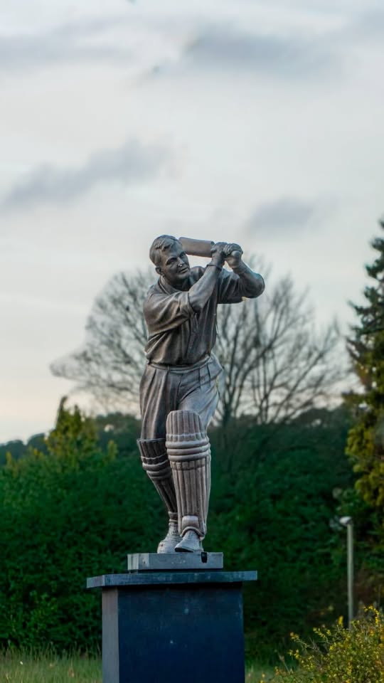 A bronze statue of a vintage male cricket batsman captured mid-swing