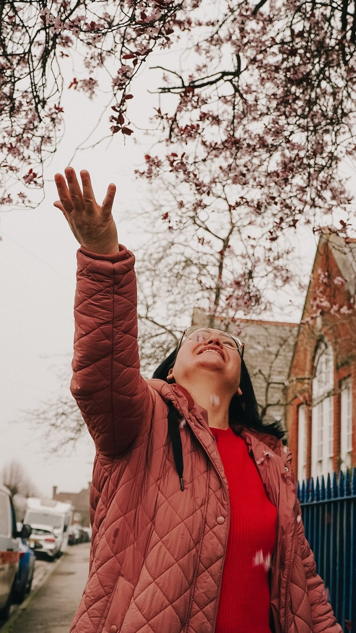 Smiling woman with glasses reaching toward pink cherry blossoms